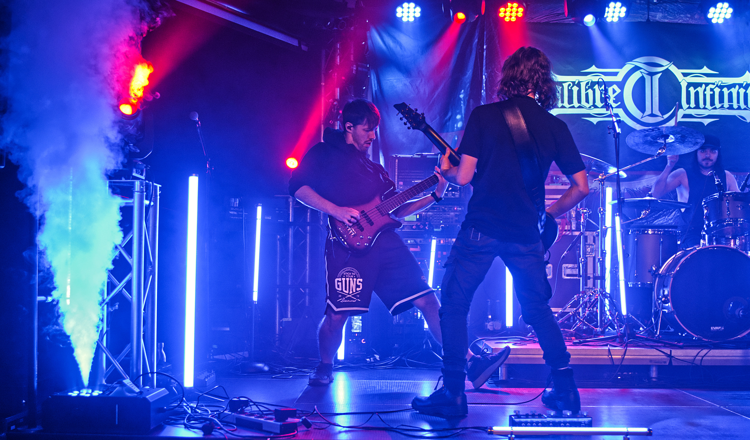 Bass and guitar duo on stage in blue light and smoke