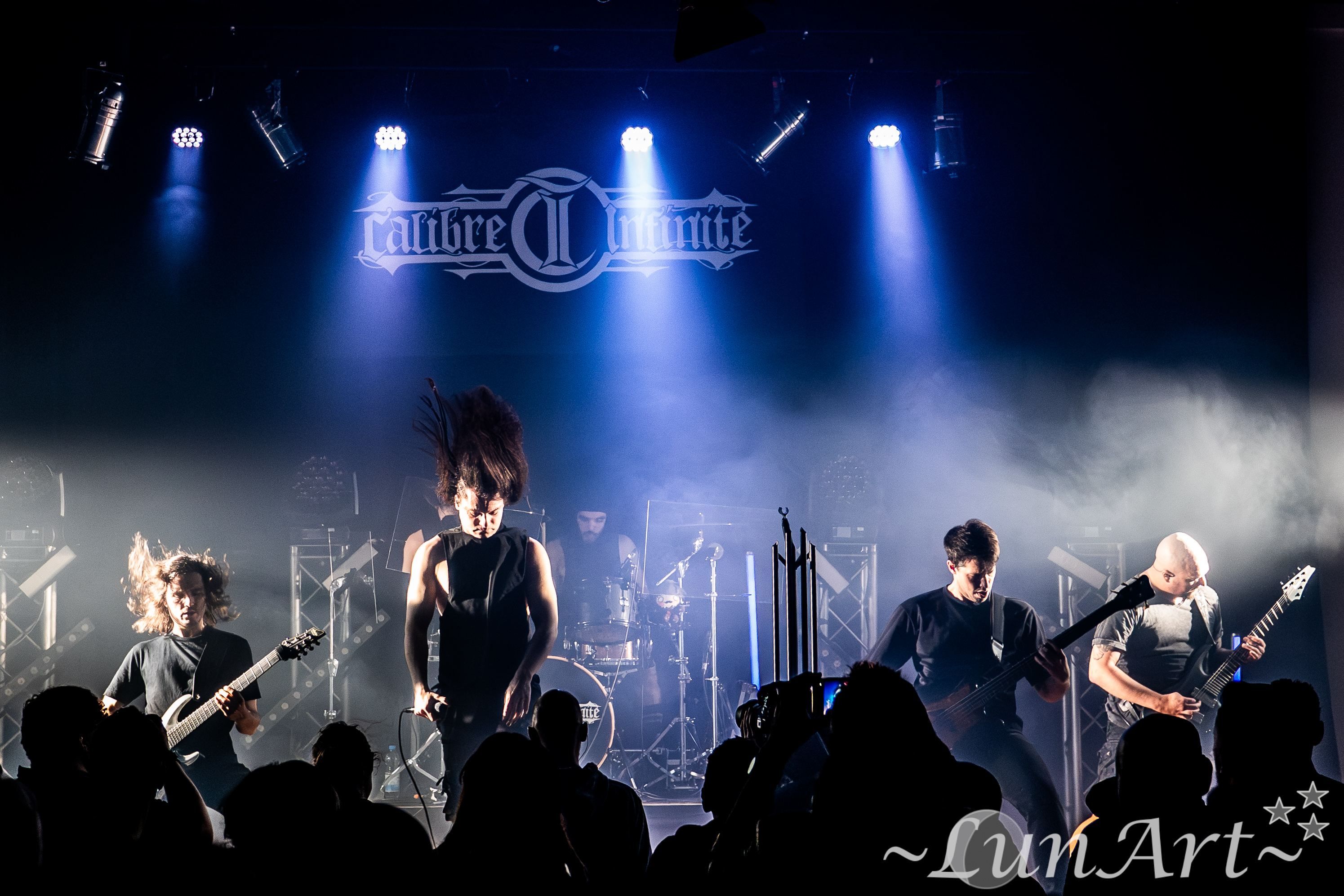 Full-band live hero shot with crowd silhouettes and stage banner